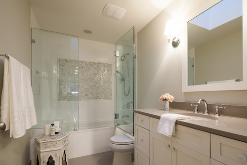 Modern bathroom with double vanity, glass-enclosed shower, towel rack, and small decorative table by the toilet with flowers on the counter.