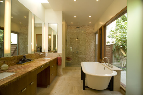 Spa-like bathroom with a double vanity, marble countertop, and large mirrors on the left; freestanding tub by a window on the right and a glass-enclosed shower at the back.