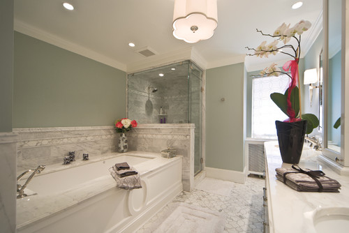 Luxurious marble bathroom with a large freestanding tub, glass shower, pale green walls, and orchids on the counter.