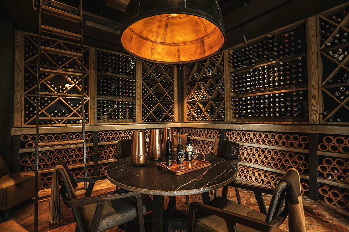 Dimly lit wine cellar with a round table, decanters, and bottles stored on wooden racks.